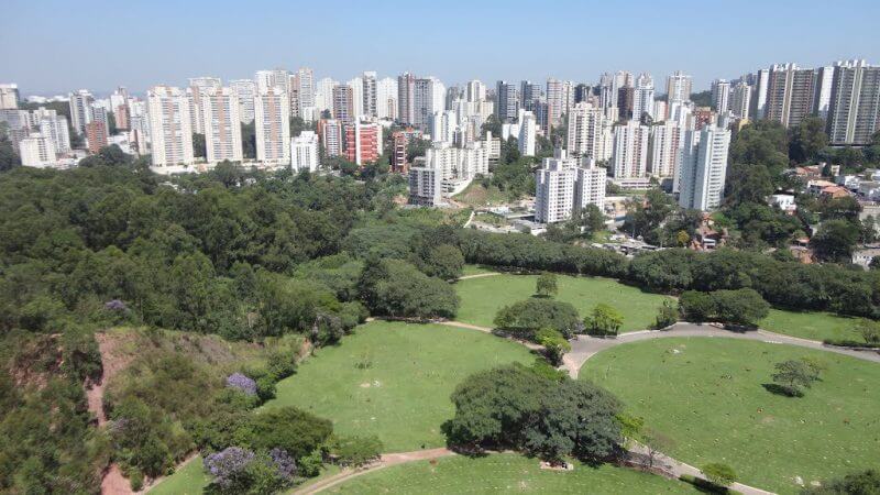 Imagem aérea di bairro Vila Andrade, em dia de céu claro, com muitos prédios ao fundo e um parque a frente.