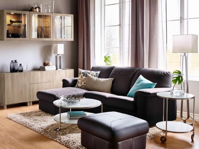 Sala de estar, em que se vê um sofá preto com almofadas coloridas em cima, uma mesa de centro e um armário
