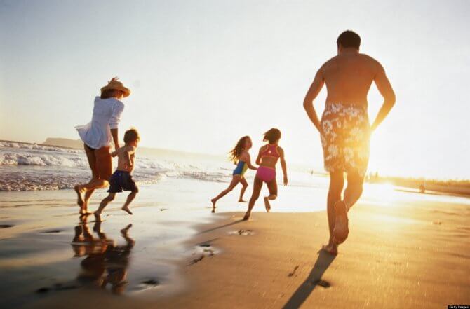 Família com um homem, uma mulher e três crianças, duas meninas e um menino, ele segurando a mão da mãe, correndo juntos na areia da praia ao pôr do sol 