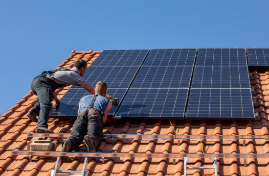 Dois homens instalando painéis solares em uma residência.